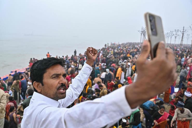 מתפלל הינדי מצלם סרטון בטלפון הנייד שלו בזמן שעולי רגל מתאספים לטבול במים הקדושים של סנגם, מקום מפגשם של הנהרות גנגס, ימונה ונהר סרסוואטי המיתולוגי, במהלך פסטיבל מאהה קומבה מלה בפריאגרג'