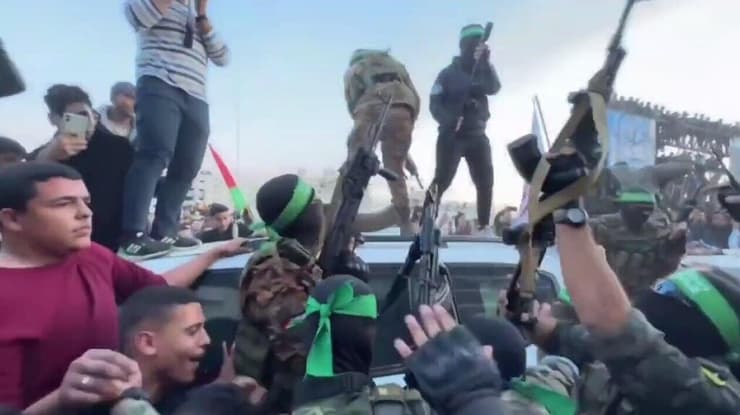 מחבלי חמאס מטפסים על רכבי הצלב האדום בעת העברת החטופו