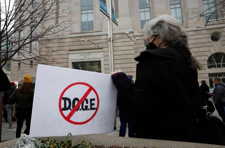 מפגינה עם שלט נגד המשרד ליעילות ממשלתית DOGE של אילון מאסק כחלק ממחאה נגד סגירת סוכנות הסיוע לפיתוח בינלאומי של ארה"ב סיוע הומניטרי זר USAUD ב וושינגטון מחוץ למטה שלה