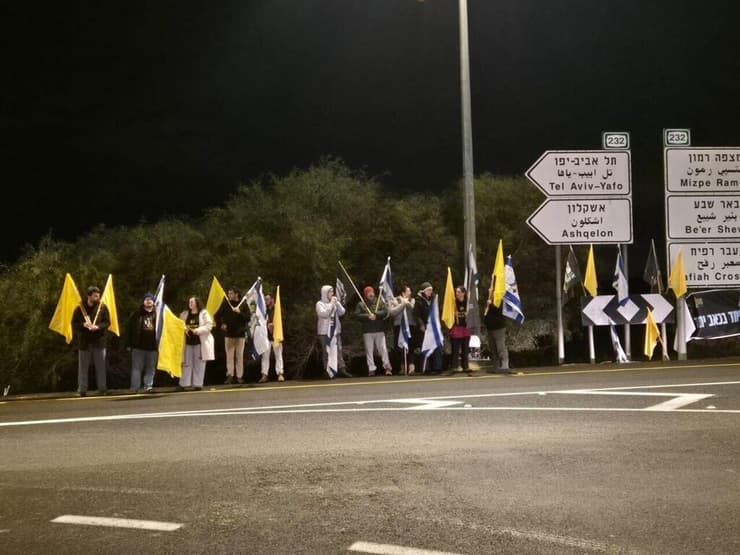 עשרות עם דגלי ישראל ודגלים צהובים, מחכים לצאת השיירה אזרחים תומכים בצומת גמה במהלך קבלת ארונה של שירי ביבס והעברתו לאבו כביר