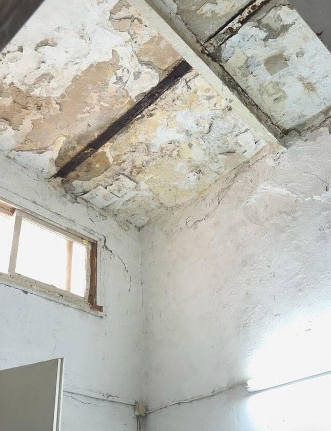 קירות מתקלפים, תקרה שחושפת את היסודות הפנימיים של הבניין, וחלונות שבורים. ביתה המתפורר של בתיה    