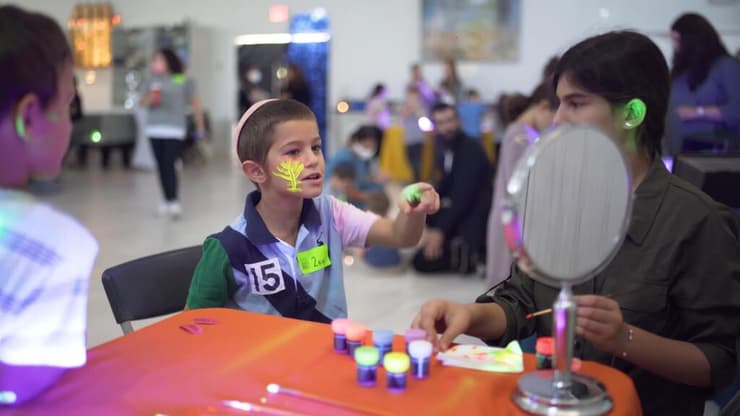 נער צעיר צובע את פניו בצבעים זוהרים בחושך במהלך אירוע קהילתי שנערך על ידי הקהילה היהודית בפאלם ביץ'