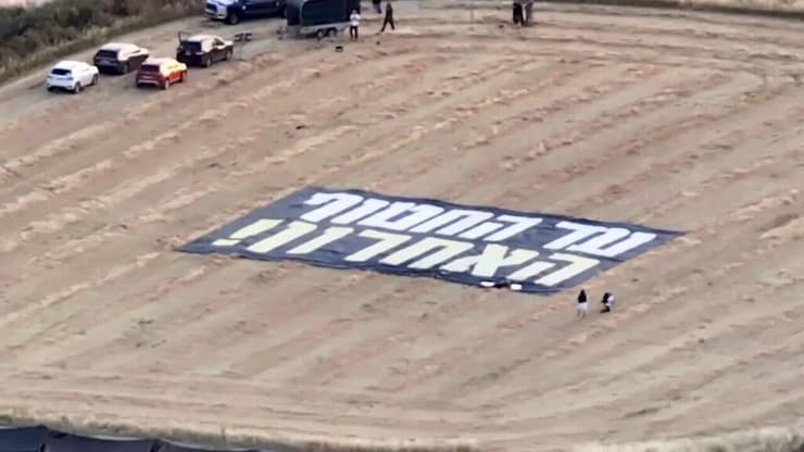 השלט הענק שפרסו המוחים במושב (צילום: אביב אטלס Aviv Atlas) שלט להחזרת החטופים בשדה במזור מול בית משפחת ירדני שבו יחגוג נתניהו את המימונה