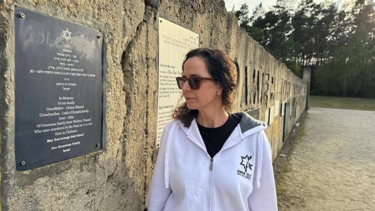 פרופ' רחל גרוסמן מביטה בשלט לזכר סבה, סבתה ודודתה, שנרצחו על ידי הנאצים, במחנה ההשמדה חלמנו שבפולין