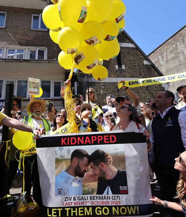 דמארי מפריחה בלונים צהובים, על רקע שלט שקורא לשחרורם של זיו וגלי ברמן (צילום: Reuters/Paul Childs) אמילי דמארי מחוץ לאצטדיון טוטנהאם