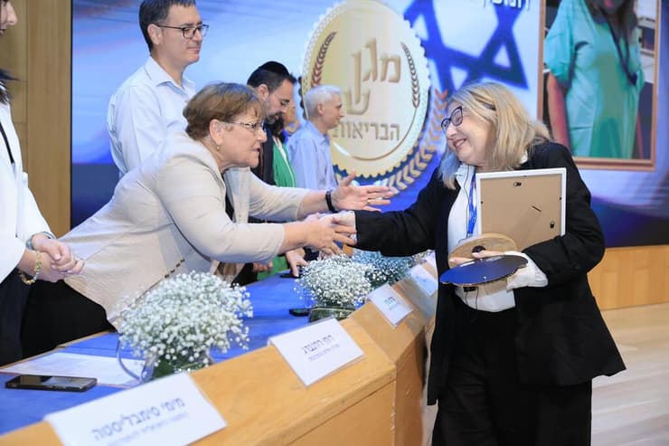 ד"ר שלי טפר בעת קבלת אות מגן שר הבריאות להתנדבות מיו"ר הוועדה המייעצת למגן ההתנדבות, מרים פרץ (צילום: אסי אפרתי) ד"ר שלי טפר מתנדבת במכון לרפואה משפטית קיבלה אות מגן שר הבריאות להתנדבות