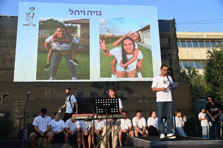 אלי שרעבי נואם בעצרת, כשמאחוריו תמונות נויה ויהל ז"ל (צילום: יאיר שגיא) אלי שרעבי בעצרת "הקול שלנו" של בני הנוער מקיבוץ בארי בכיכר החטופים