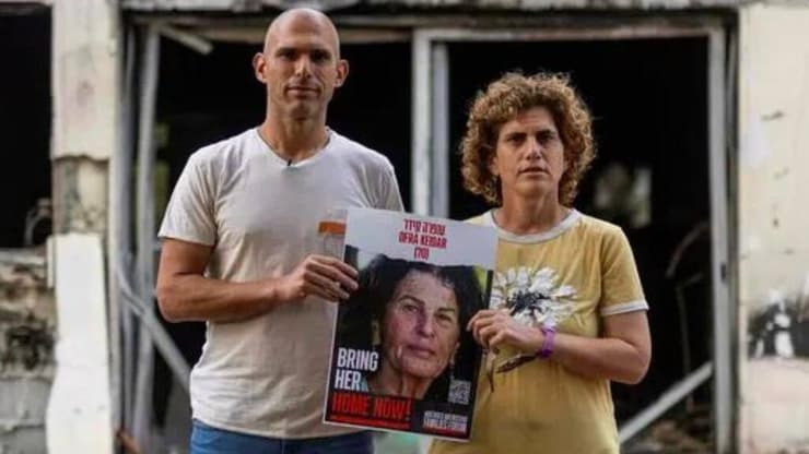 יעל ואלעד קידר, ילדיה של עפרה קידר ז"ל, על רקע ביתה השרוף (צילום: דוברות קיבוץ בארי) יעל ואלעד קידר, ילדיה של עפרה קידר ז"ל, על רקע ביתה השרוף