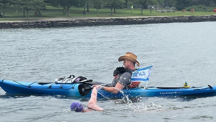 דבי במהלך השחייה, ולצידה סירה עם דגל ישראל ועליו מתנוססת תמונתו של ירון ז"ל   