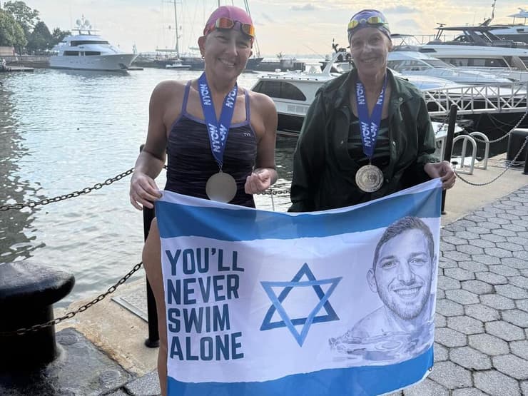 דבי (מימין) עם ענת אחימאיר אשחר, שותפתה לשחייה, אוחזות בדגל עם תמונתו של ירון ז"ל. "ירון תמיד איתי"    
