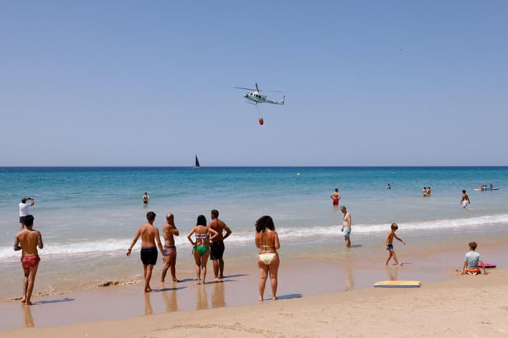 מתרחצים מביטים במסוק כיבוי אזור העיר טריפה ב ספרד שריפה שריפת יער