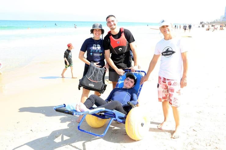 עדי בכסא גלגלים מיוחד עם מתנדבי "הגל שלי". "מנרמל עבור הילדים את המגבלה שלהם" (צילום: דנה קופל) ילדים מאובחני דושן-בקר מעמותת "צעדים קטנים" גולשים בבת ים עם מתנדבי עמותת "הגל שלי"