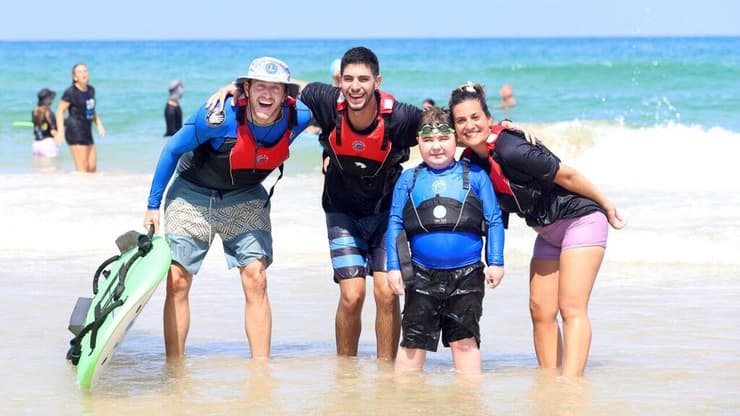 דניאל יחד עם המתנדבים. "כיף לי לגלוש" (צילום: דנה קופל) ילדים מאובחני דושן-בקר מעמותת "צעדים קטנים" גולשים בבת ים עם מתנדבי עמותת "הגל שלי"