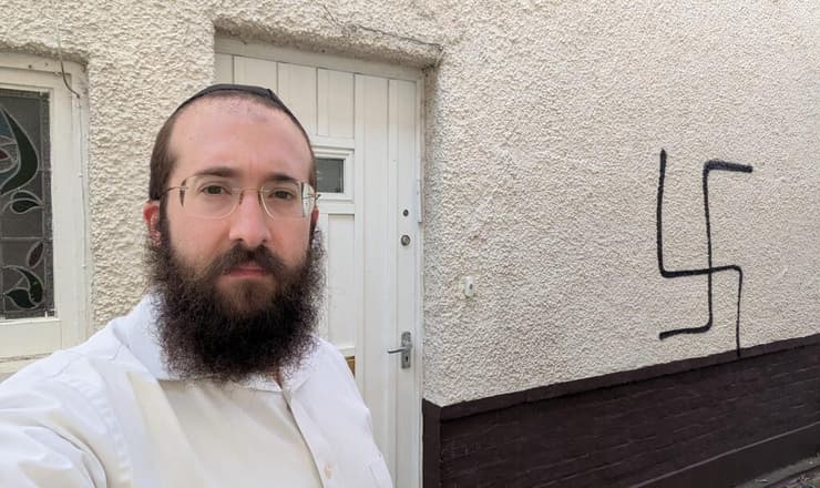 הרב בנצי אלפרוביץ' לצד הגרפיטי של צלב קרס שרוסס על ביתו