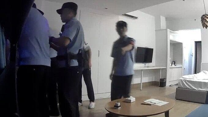 ארבעה שוטרים מנסים לכבות את המקרן, חמישי מצביע על המצלמה שבה מתעד אותם "המורד" צ'י מבריטניה מחאה נגד המפלגה הקומוניסטית על בניין ב סין הקרין וברח