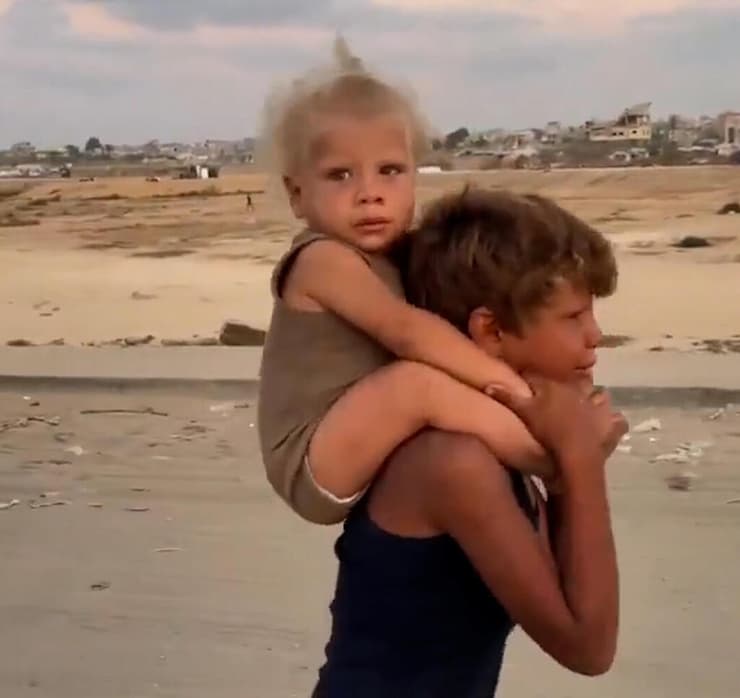 ילד צעיר בשם ג'דוע סוחב את אחיו על גבו בדרך א-רשיד ברצועת עזה