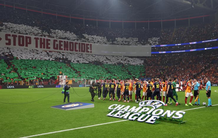 שחקני גלאטסראיי על רקע השלט הפרו-פלסטיני (צילום: REUTERS/Umit Bektas) אוהדי גלאטסראיי עם תפאורה של דגל פלסטין ושלט נגד ישראל