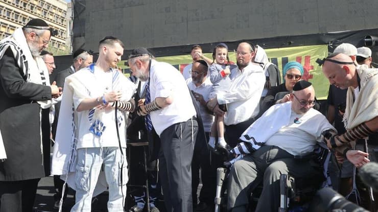 האב טל (מימין בכיסא הגלגלים) נעמד כדי לברך (צילום: מוטי קמחי) שורד השבי בר קופרשטיין הגיע לכיכר החטופים לאירוע הנחת תפילין