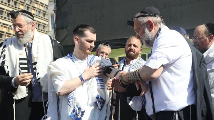 "הגשמת חלום". בר קופרשטיין מניח תפילין על הבמה בכיכר החטופים (צילום: מוטי קמחי) שורד השבי בר קופרשטיין הגיע לכיכר החטופים לאירוע הנחת תפילין