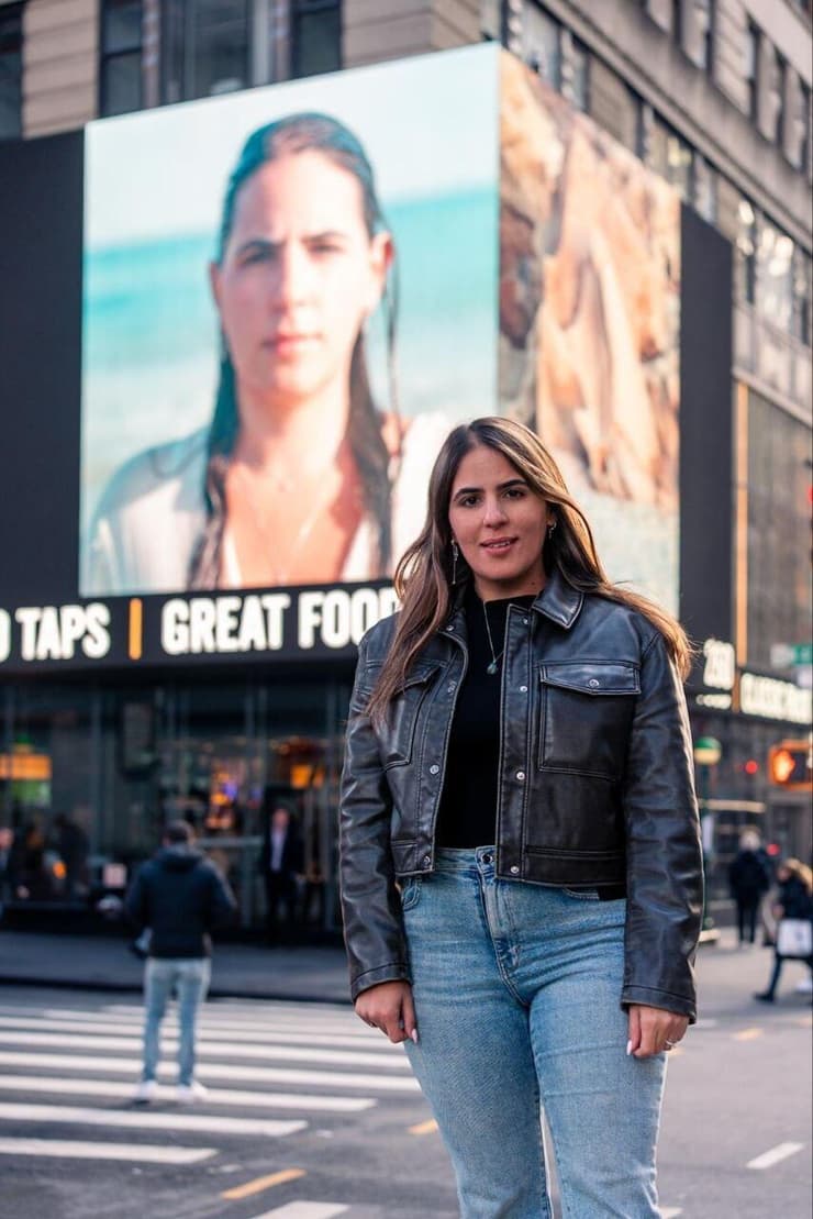 עדן שמואל ניצולה מטבח מסיבת הנובה עם תמונתה על גבי בילבורד ב"טיים סקוואר", ניו יורק