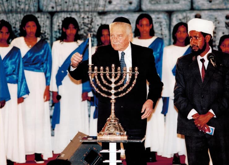 עזר ויצמן, נשיאהּ השביעי של ישראל, מדליק נר ראשון של חנוכה בחנוכייה (צילום: באדיבות בית הנשיא) עזר ויצמן, נשיאהּ השביעי של מדינת ישראל, מדליק נר ראשון של חנוכה בחנוכייה של משפחת ימיני