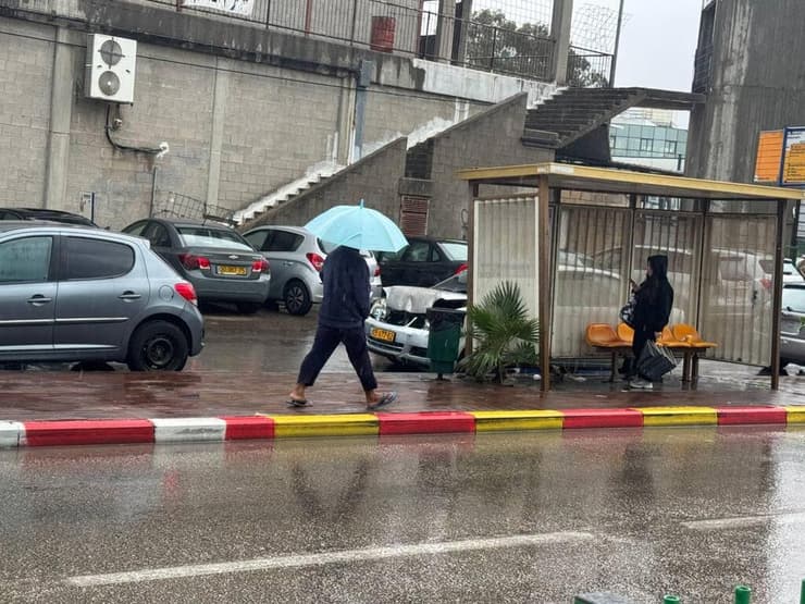 עם מטרייה וכפכפים, באור עקיבא (צילום: איתן גליקמן ) אור עקיבא: תושב המקום בגשם הסוער עם מטרייה וכפכפים - סופת ביירון