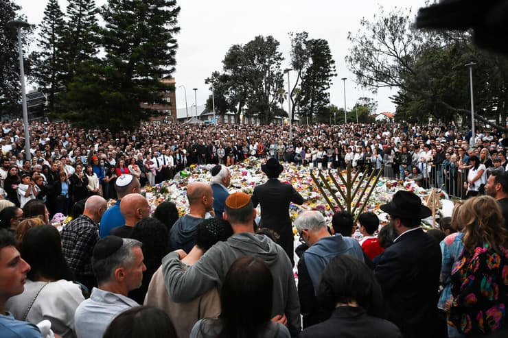 המונים התאספו היום בזירת הטבח, הניחו פרחים לזכר הקורבנות והדליקו חנוכייה (צילום: REUTERS/Flavio Brancaleone) מחווה בזירת טבח סידני אוסטרליה בונדיי ביץ' עם דגל ישראל לקורבנות פיגוע ב חנוכה