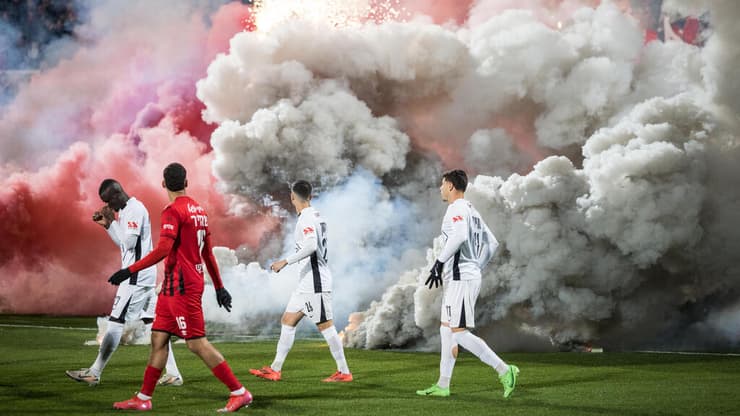 שחקני הפועל תל אביב על רקע רימוני עשן במשחק רבע גמר גביע המדינה מול הפועל רמת גן. אצטדיון רמת גן, 25 בפברואר 2025