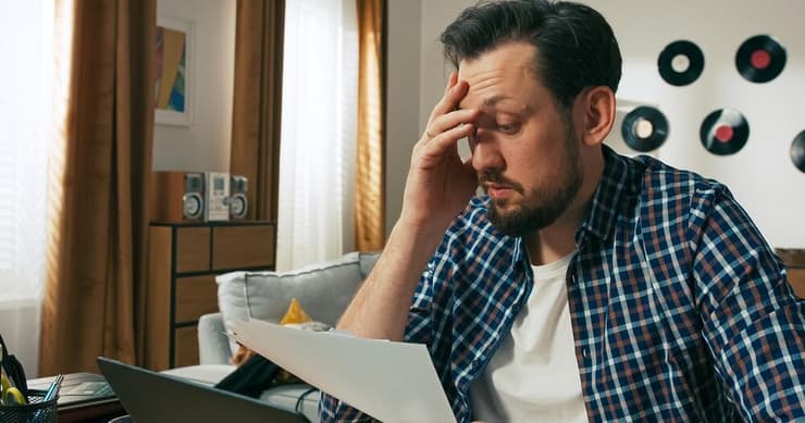 "כל החכמה היא בתכנון" (צילום: Shutterstock) גבר יושב בסלון לבד מביט בדף ונראה מודאג