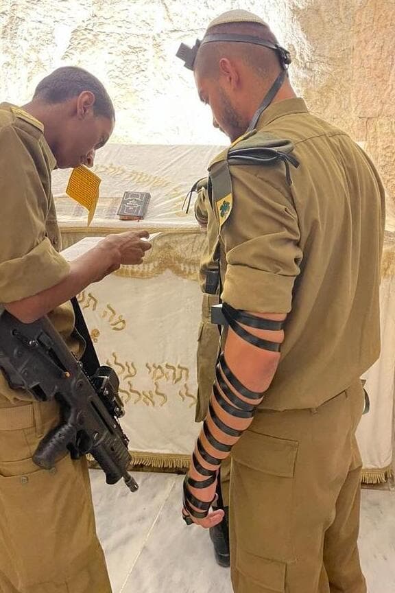 אדיר בוגלה (משמאל) מניח תפילין עם חברו. "שבועיים לפני שנפל, הוא חילק ציציות לחברים ואמר שזה 'השכפ"צ שלהם'" (באדיבות המשפחה) אדיר בוגלה מניח תפילין עם חברו