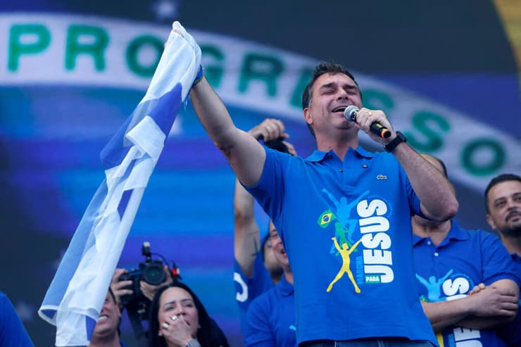 בולסונרו הבן מניף את דגל ישראל על הבמה בתחילת יוני (צילום: Miguel SCHINCARIOL / AFP) ברזיל סנאטור פלביו בולסונרו פלאביו בולסונרו בנו של ז'איר בולסונרו עם דגל ישראל ב עצרת יוני 2026 צעדה למען ישו