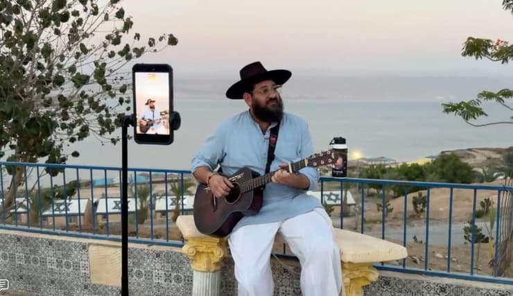 מוזיקאי מופיע במהלך שידור חי ברשתות החברתיות, על רקע ים המלח, בזמן שמשתתפי תוכנית Storytellers של תגלית ישראל יוצרים תכנים לאורך המסע שלהם (צילום: באדיבות תגלית ישראל) A musician performs during a live social media broadcast overlooking the Dead Sea as participants in Birthright Israel’s Storytellers program create content throughout their trip