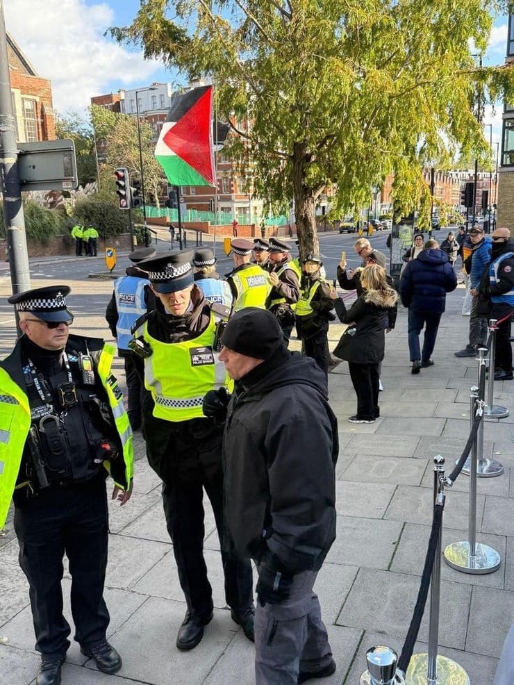 Police officers stand outside the London venue hosting aliyah events as a Palestinian flag is displayed nearby during a pro-Palestinian demonstration 