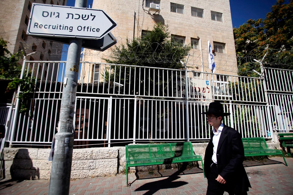 An ultra-Orthodox man walks past a sign for an IDF recruitment office 