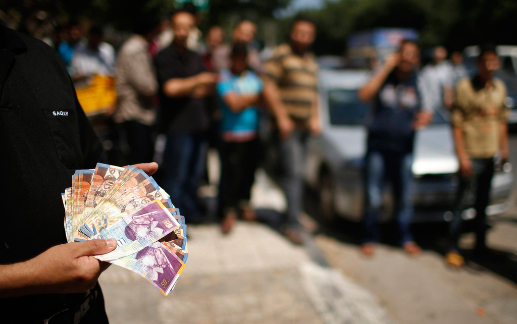 Palestinian showcases bank notes outside Gaza Strip bank, July 17, 2014 