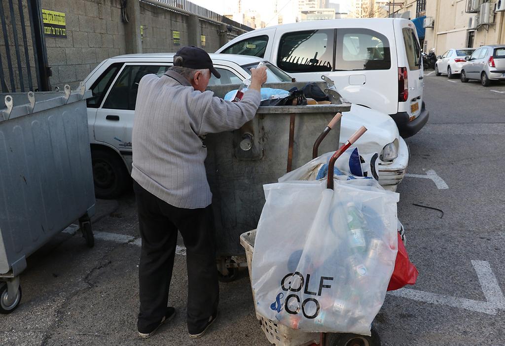 An elderly Israeli man searches in the trash for empty bottles that can be returned to stores for a small amount of money 