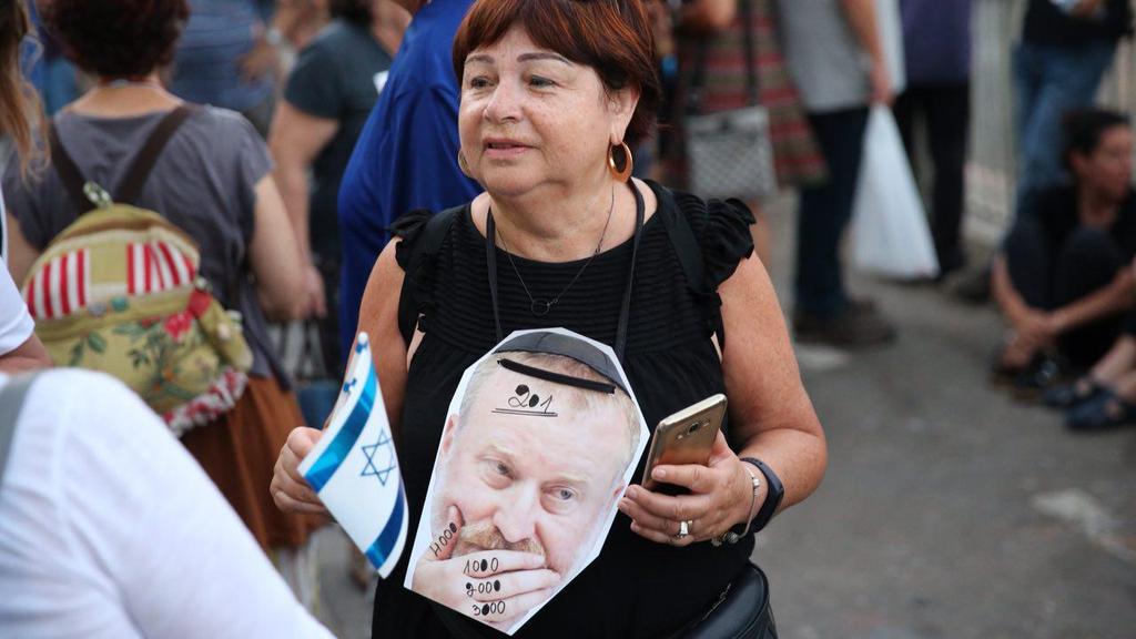 Woman holds cut put of Mandelblit's face during pro-Netanyahu demo outside AG's house 