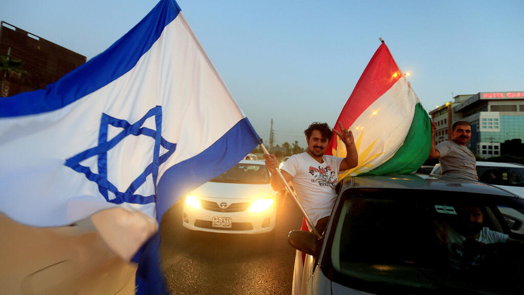A Kurdish man holding Israeli and Kurdish flags

