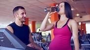 אישה בהיריון שותה מים בחדר הכושר