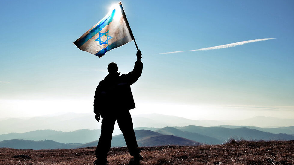 A man flying the Israeli flag (Photo: Shutterstock) היינו פה: הנפת ותקיעת דגל על פסגת ההר