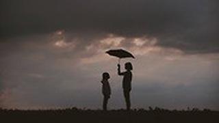 ילדה גדולה מצלה במטריה על ילדה קטנה במזג אוויר חורפי וגשום 