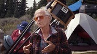 ג'ון דובסון על רקע טלסקופ מקצועי שנבנה בהשראתו. 