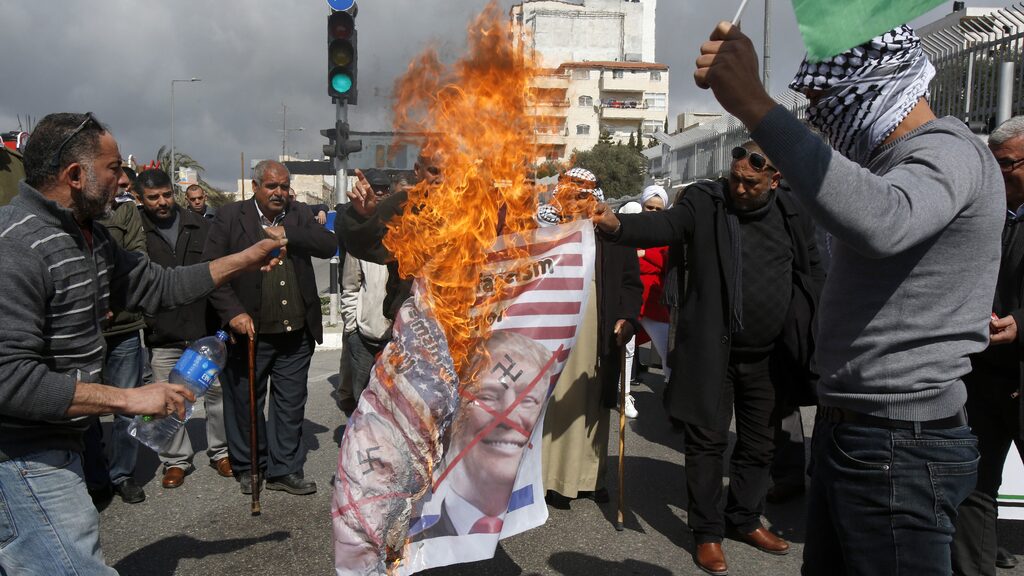 Palestinians in Bethlehem burn a banner depicting U.S. President Donald Trump and Prime Minister Benjamin Netanyahu to protest Israel’s decision to withhold tax revenue owed to the PA, Feb. 19, 2019 
