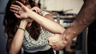 אשה מכסה את הפנים בידיים, גבר עם אגרוף קפוץ לידה עומד להכותה 