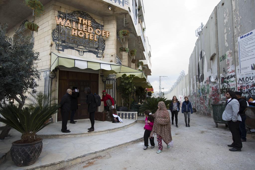 People pass by the The Walled Off Hotel located next to the Israeli security barrier in the West Bank city of Bethlehem
