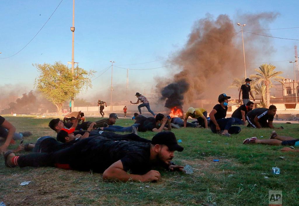 Anti-government protesters take cover during a demonstration in Baghdad, Iraq, as security forces open fire 