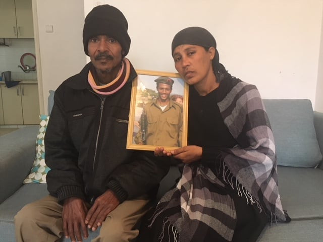 Atalay and Mamey Biadga sit in their Lod living room with a picture of their son, Yehuda, who was killed a year ago by police.