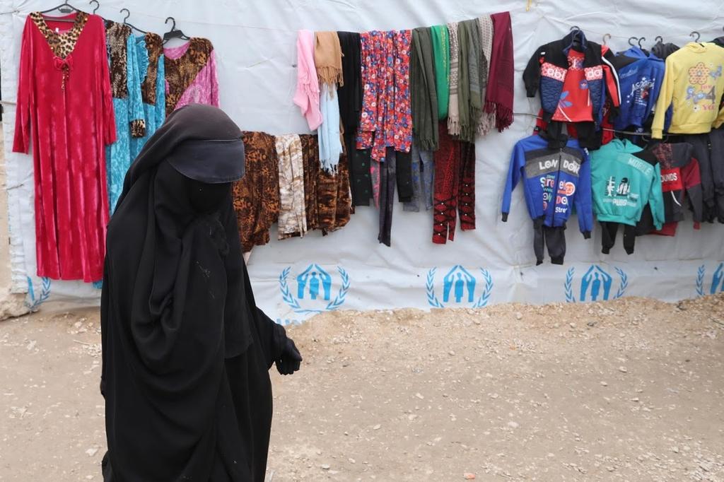 A woman walks past hung up clothes in al-Hol camp 