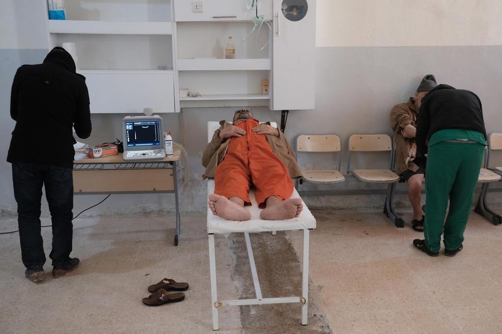 A foreign prisoner lies on top of an examining table next to a doctor inside a prison in Hasaka 