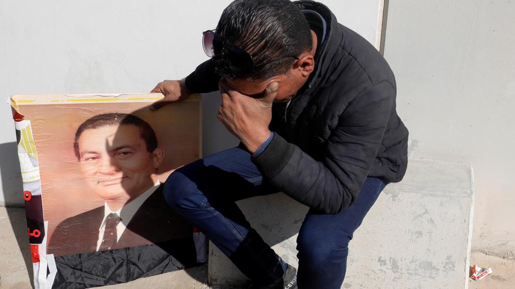 A supporter of Hosni Mubarak holds a photo of the former Egyptian president outside the mosque east of Cairo where his funeral will be held, Feb. 26, 2020 